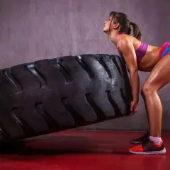 Kobieta w sportowym stroju podnosi dużą oponę w siłowni.